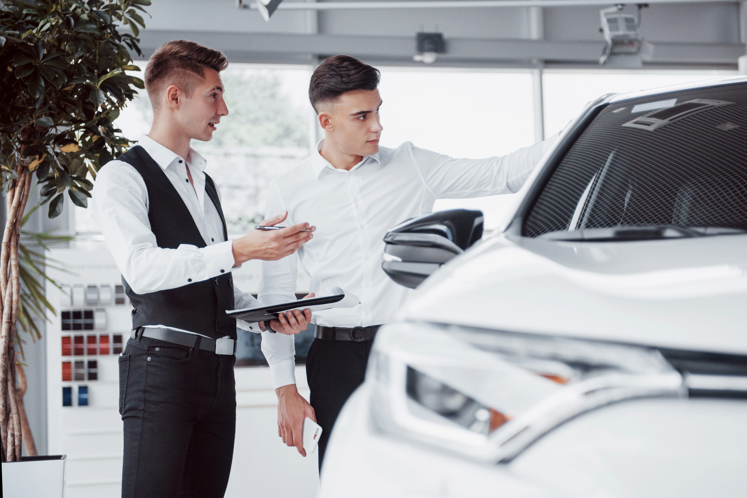 Two men stand in the showroom against cars. Close-up of a sales manager in a suit that sells a car to a customer.